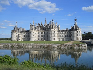 chateau de Chambord en été reflet dans les eaux du Cosson affluent de la Loire canalisé herbe verte fleurs blanches, ciel bleu et nuages blancs