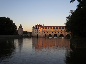 La nuit à Chenonceau : forêt, donjon et belle lumière orangée sur la façade en tuffeau du château-pont dont la galerie surplombe le Cher